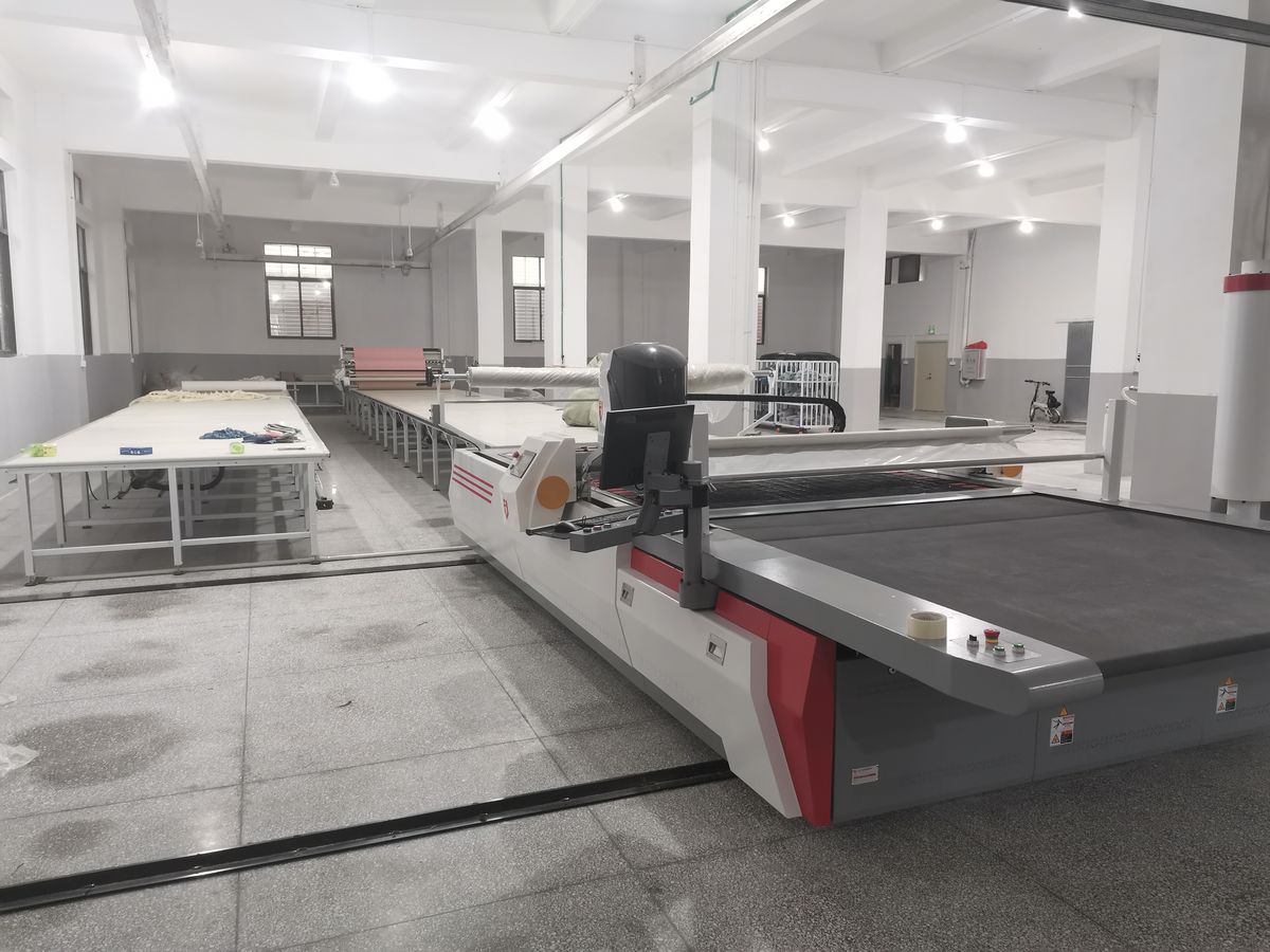 An automated fabric cutting table in the cutting room, with spreading tables behind it.