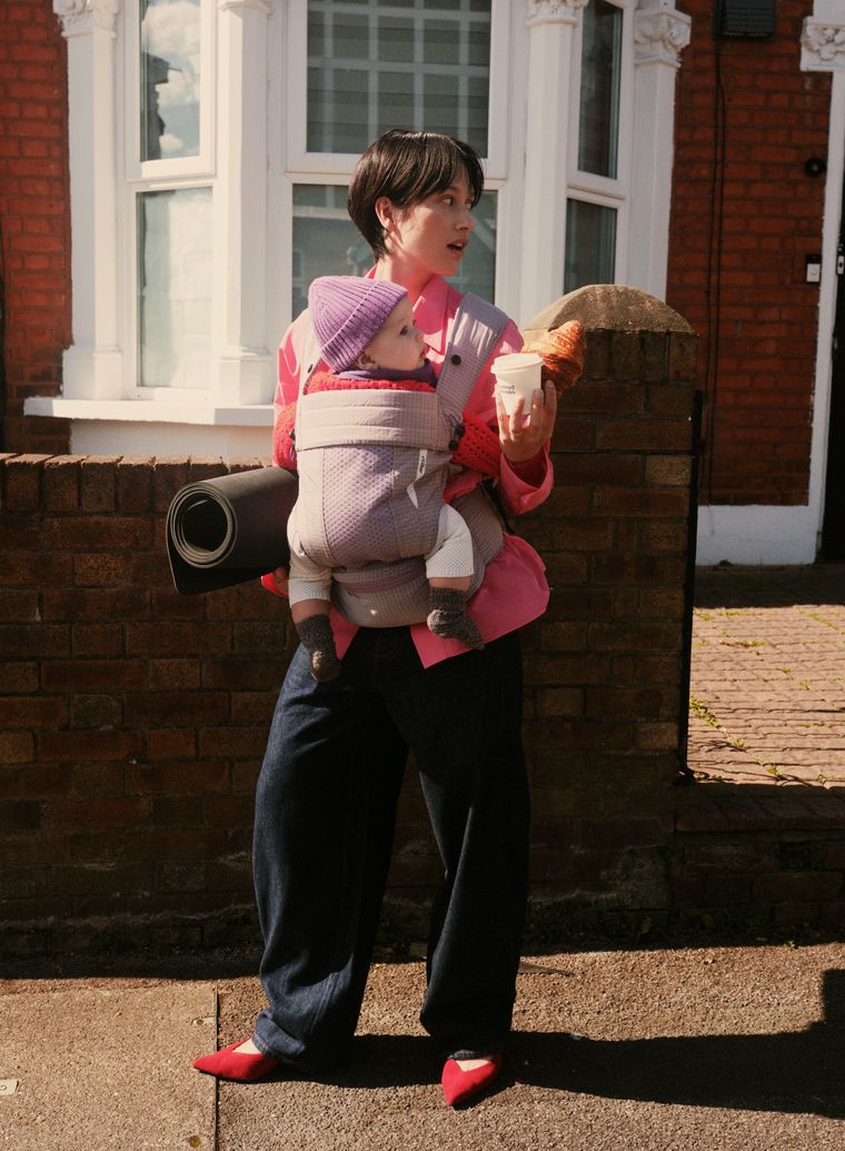 A parent carrying a baby and a rolled mat on a London street